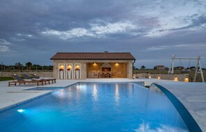 Une piscine avec un bâtiment en pierre en arrière-plan, un patio avec des chaises longues et une vue sur la campagne.