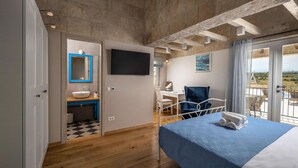 Ein Schlafzimmer mit Bett, Schreibtisch, Stuhl, einem Badezimmer mit Waschbecken und Spiegel sowie einem Balkon mit Blick.