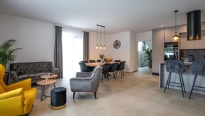 Ein modernes Wohnzimmer mit einer Couch, Sesseln, einem Esstisch und einer Küchenzeile.