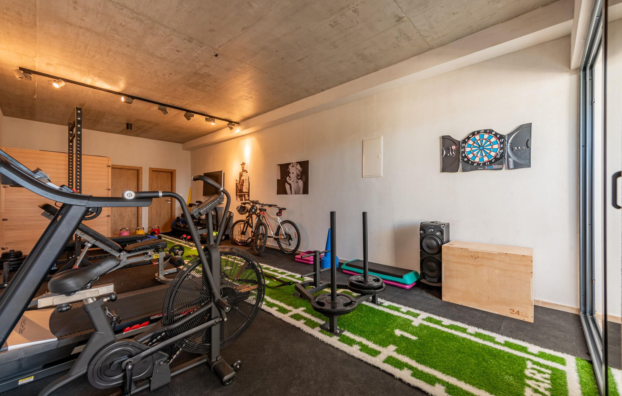 Et hjemmegym med træningsudstyr, en grøn græstæppe og en dartskive på væggen.