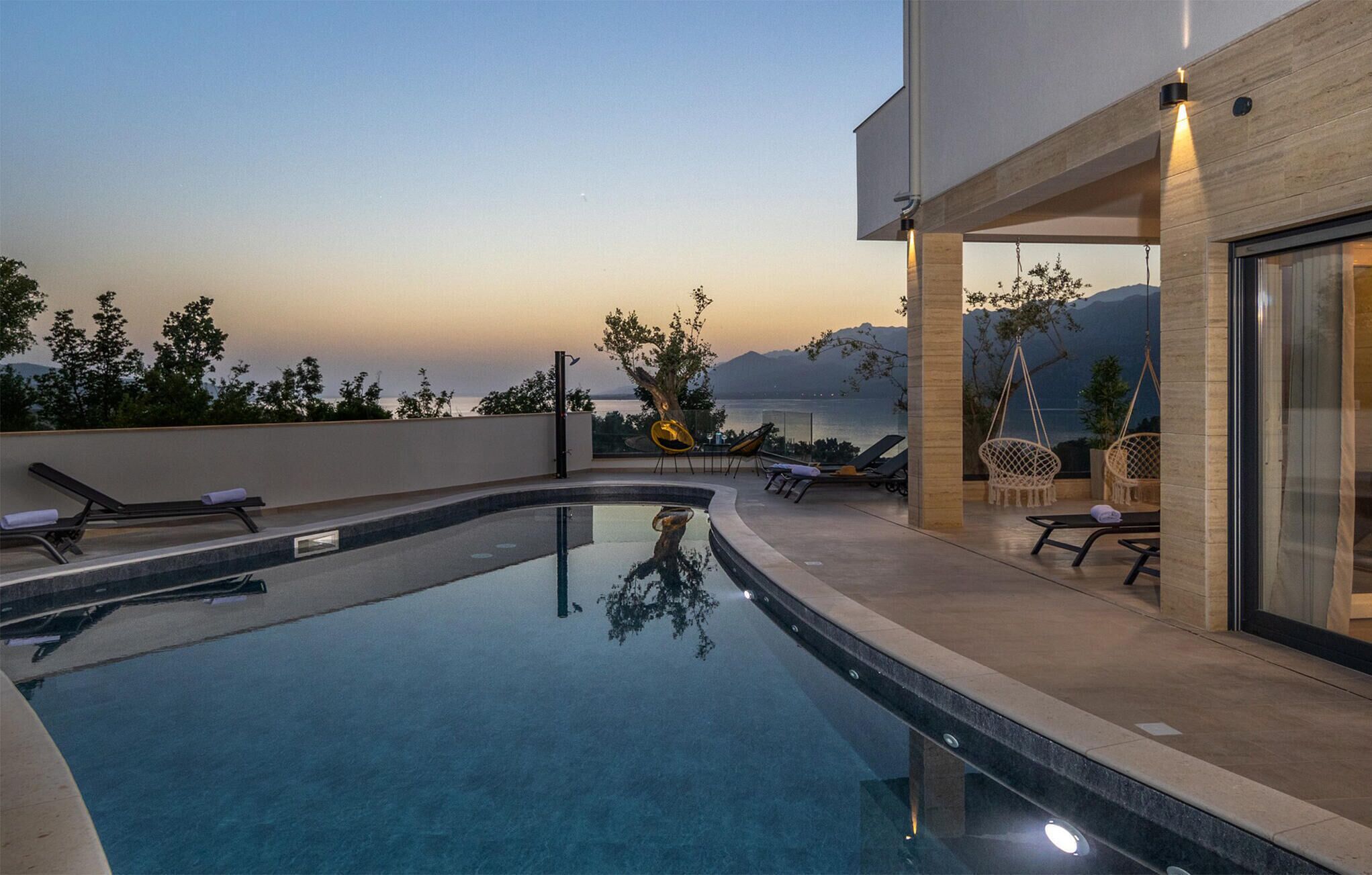Un área de piscina moderna al aire libre con sillones de descanso y vistas al mar y a las montañas.