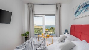 A bedroom with a bed, a bedside table with a tray of orange juice, a lamp, and a view of the sea and hills. - Stunning home in Rovanjska with sauna (Rovanjska)