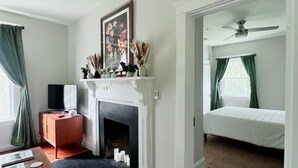 A room with a fireplace, a bed, a television, and a door leading to another room. - Hometract Cottage, Historic Property, UVA/Charlottesville/Ivy (Charlottesville)