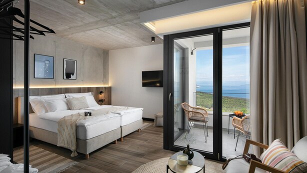 A modern bedroom with a large bed, a TV, and a balcony with wicker chairs. - Luxurious home in Crni (Crni)