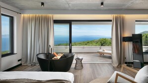A modern hotel room with a large bed, a black bathtub, a small table with a towel, a chair, and a view of the sea. - Luxurious home in Crni (Crni)