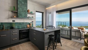 A modern kitchen with a large island, dark cabinetry, and a view of the sea through a large window. - Luxurious home in Crni (Crni)