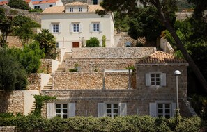 A stone building with multiple windows and shutters, surrounded by trees and other buildings. - Villa Paxos Palace (Orti) (Dubrovnik)