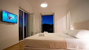 Une chambre à coucher avec un lit, un téléviseur fixé au mur et une porte donnant sur un balcon.