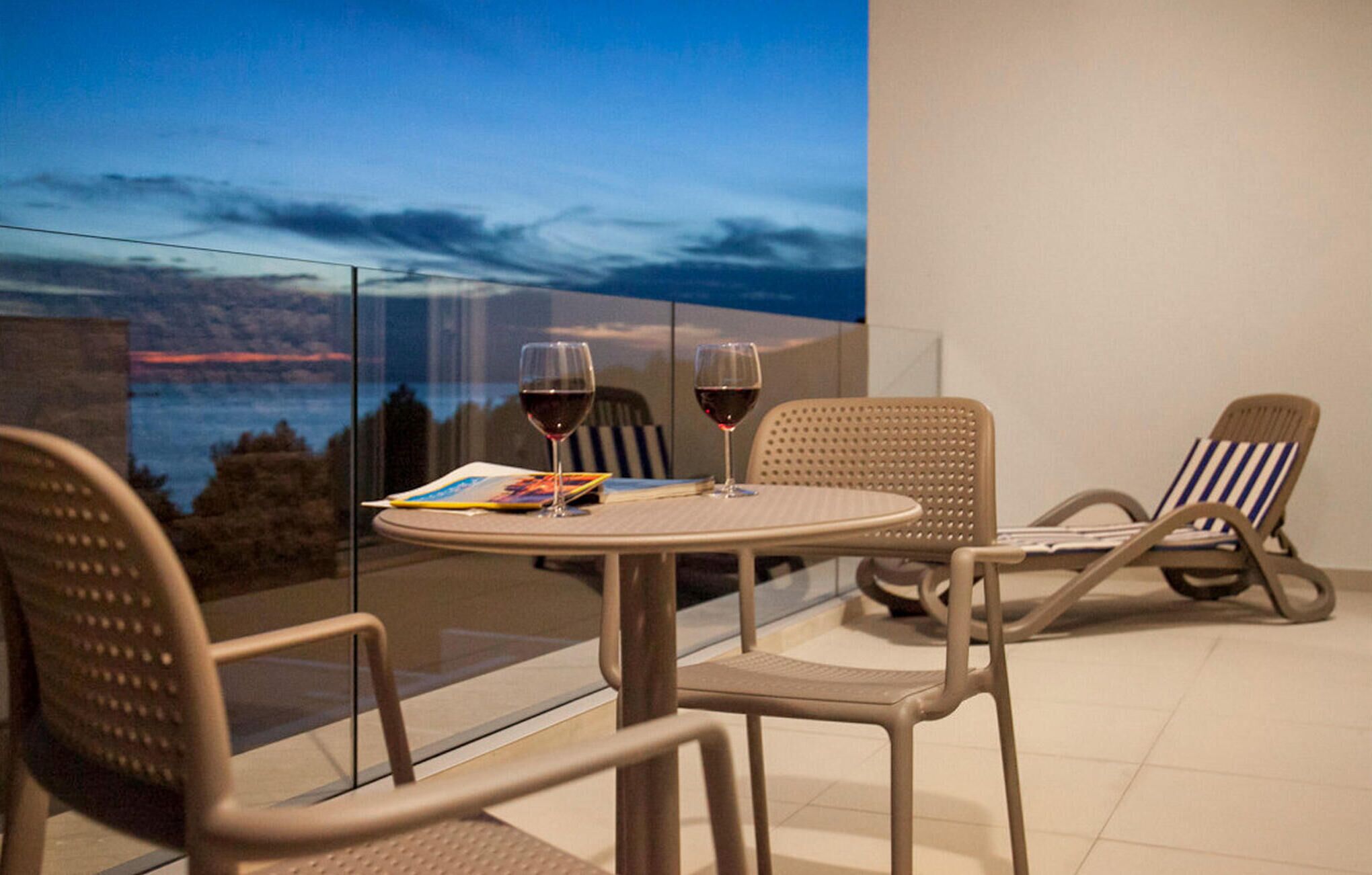 A balcony with a table and two chairs, two glasses of red wine, and a book.