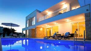 Une maison moderne à deux étages, dotée d’une piscine, de chaises longues et d’un parasol.