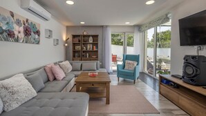 Ein modernes Wohnzimmer mit grauem Sofa, einem Holztisch, einem Bücherregal, einem blauen Sessel und einem Flachbildfernseher.