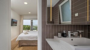 Ein modernes Badezimmer mit einem großen Waschbecken, einem Spiegel und einem Fenster mit Blick auf Grünflächen.