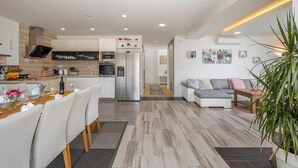 Eine moderne Küche mit Kochinsel, ein Essbereich mit Tisch und Stühlen, ein Wohnzimmer mit Sofa und Couchtisch sowie ein Flur, der zu einem weiteren Raum führt.
