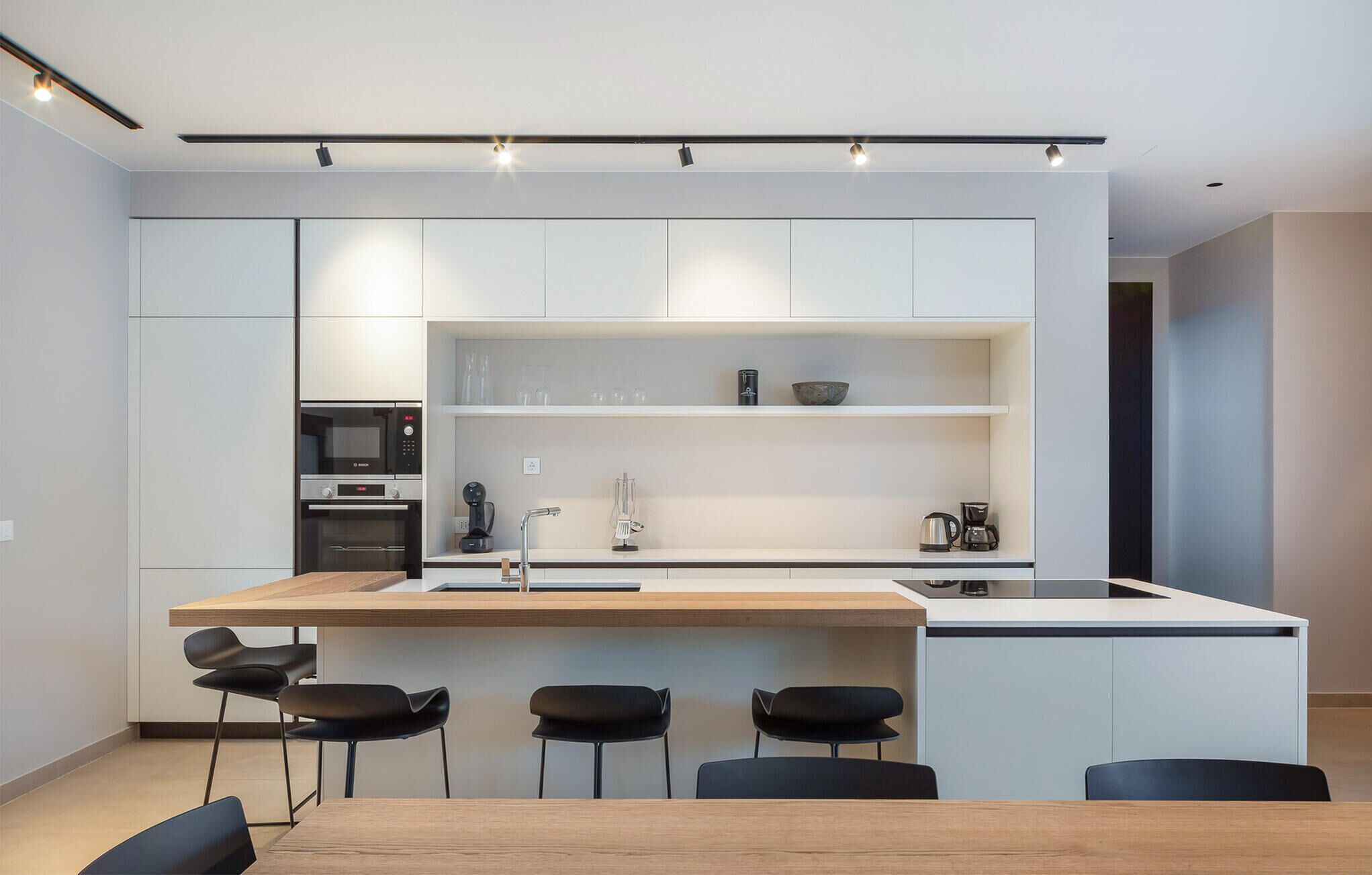 A modern kitchen with white cabinetry, a wooden island, and black chairs.