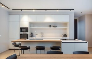 A modern kitchen with white cabinetry, a wooden island, and black chairs.