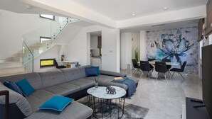 A modern living room with a grey sectional sofa, a round coffee table, and a staircase leading to an upper level. - Cozy home in Privlaka with sauna (Privlaka)