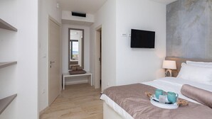 A hotel room with a bed, a TV mounted on the wall, a bedside table with a lamp, and a view of the sea through an open door. - Cozy home in Privlaka with sauna (Privlaka)