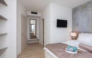 A hotel room with a bed, a TV mounted on the wall, a bedside table with a lamp, and a view of the sea through an open door. - Cozy home in Privlaka with sauna (Privlaka)