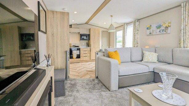 A modern living room with a grey sofa, a coffee table, and a kitchen area in the background.