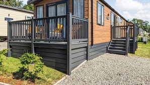A mobile home with a wooden exterior, a balcony with a black railing, and a gravel driveway.