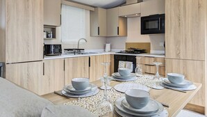 A modern kitchen with wooden cabinetry, a microwave, stove, and a dining area set with plates, bowls, and cutlery.