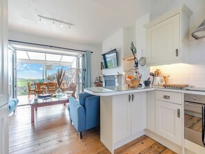A modern kitchen with white cabinets, a glass dining table, and a blue sofa.