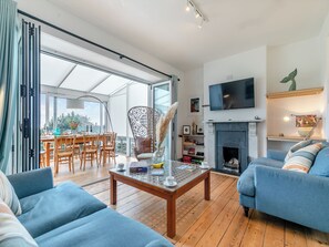A spacious living room with a fireplace, a dining area with a table and chairs, and a large TV mounted on the wall.