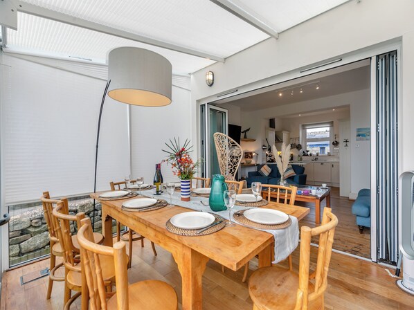 A dining area with a wooden table set for six, surrounded by chairs, a large pendant light, and a vase with flowers.