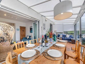 Moderni ruokailutila, jossa on pitkä puinen pöytä, johon on katettu neljälle, ja pöydän ympärillä on punottuja tuoleja.