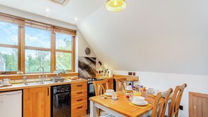 A modern kitchen with wooden cabinetry, a built-in dishwasher, and a dining area with a wooden table and chairs. - 2 bedroom accommodation in Foxhole, near Beauly (Foxhole, near Beauly)