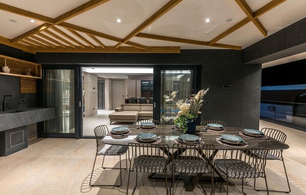 A modern dining area with a glass table, metal chairs, and a dark interior.