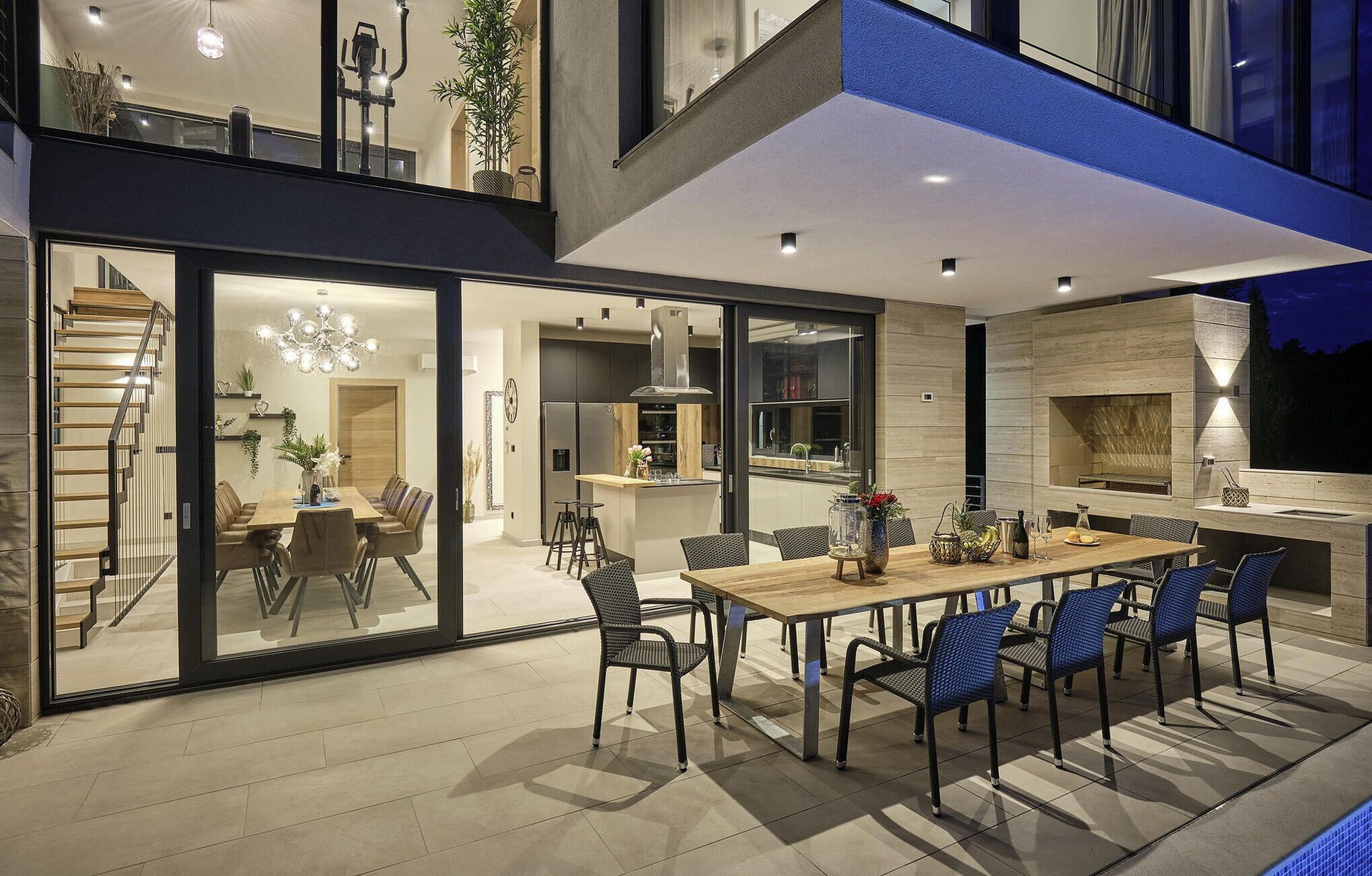 Un espacio moderno para comer al aire libre con una mesa de madera y sillas azules, junto a una cocina y un comedor.