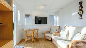 Een ruime woonkamer met houten vloer, een eettafel met stoelen, een bank en een flatscreen televisie aan de muur.
