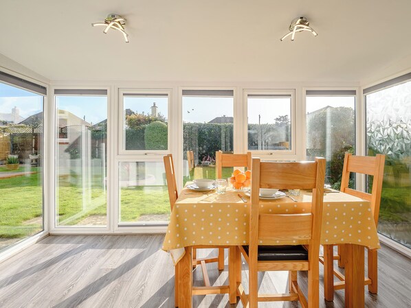 A dining area with a table set for four, large windows, and a view of a garden.