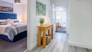 Een hotelkamer met een bed, een nachtkastje met een plant, een schilderij aan de muur en een gang naar een andere kamer.