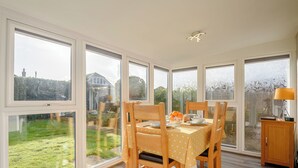 Een eetruimte met een tafel voor vier personen, grote ramen en uitzicht op een tuin en een huis.