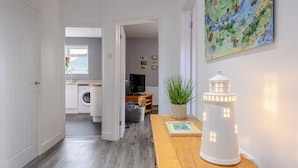 Een moderne keuken met een wasmachine, een eethoek met een houten tafel en een potplant, en een gang die leidt naar een woonkamer.