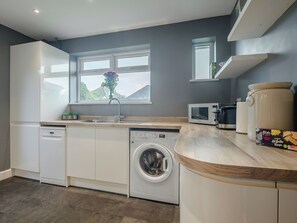 A modern kitchen with white cabinetry, a built-in washing machine, a microwave, and a large white pot.