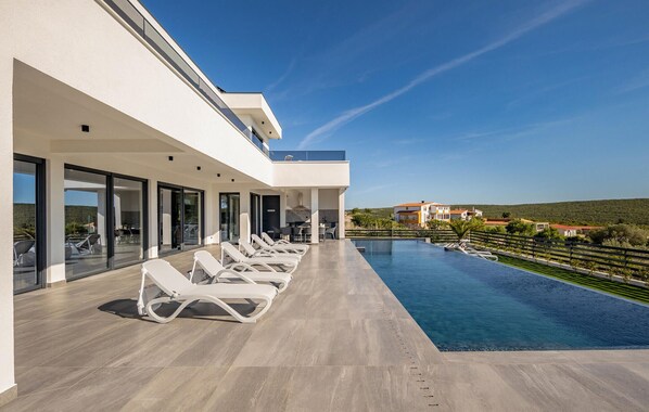 A modern outdoor swimming pool with lounge chairs, a covered patio area, and a view of the surrounding landscape. - Lovely home in Sukosan (Sukosan)