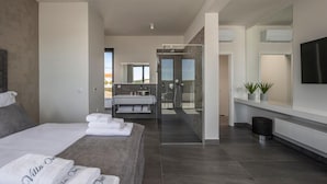 Et moderne hotelværelse med en stor seng, en glasafskærmet brusekabine, et sminkebord med spejl og et fladskærms-tv.