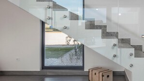 En moderne trappe med glasgelændere og geometriske mønstre, der fører op til en dør med udsigt over en anlagt have.