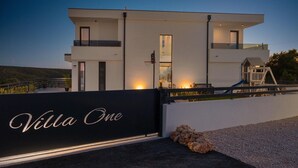 En moderne villa med en markant sort port med påskriften "Villa One", basketballbane og poolområde.