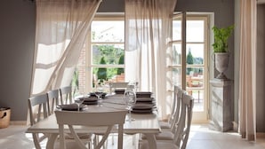 A dining area with a table set for four, white chairs, and a view of the outdoors through a large window. - Luxurious home in Bajkini (Bajkini)