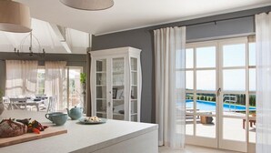 A modern kitchen with a large island, a dining area with a table and chairs, and a view of a swimming pool through a glass door. - Luxurious home in Bajkini (Bajkini)