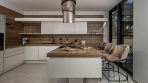 A modern kitchen with a central island, white cabinetry, and a large window providing a view of the outdoors. - Gorgeous home in Petrcane (Petrcane)