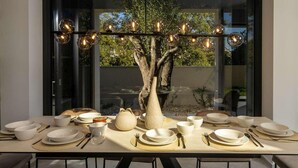 A dining table set with white plates, bowls, and cutlery, surrounded by chairs, with a tree sculpture centerpiece and a modern chandelier. - Gorgeous home in Petrcane (Petrcane)