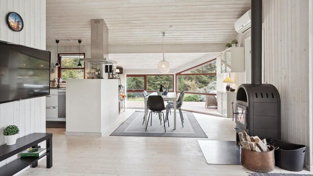 A modern kitchen with a dining area, a fireplace, and a large window overlooking greenery. - Cozy home in Hjørring with WiFi (Hjørring)