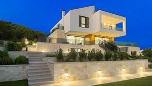 A modern two-story house with a stone facade, a staircase leading to the entrance, and outdoor lighting.