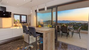 A modern kitchen with a large island, bar stools, and a dining area with a view of the sea.