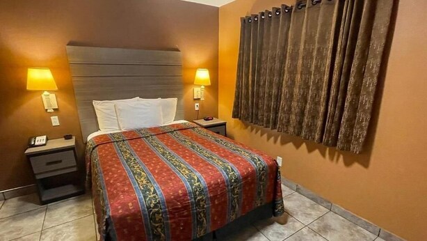Een hotelkamer met een bed, twee bedlampen, een nachtkastje en een gordijn.